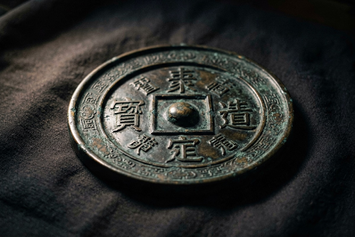 An old bronze mirror lying face-up on dark cloth, its back pattern worn smooth (AI-generated illustration)