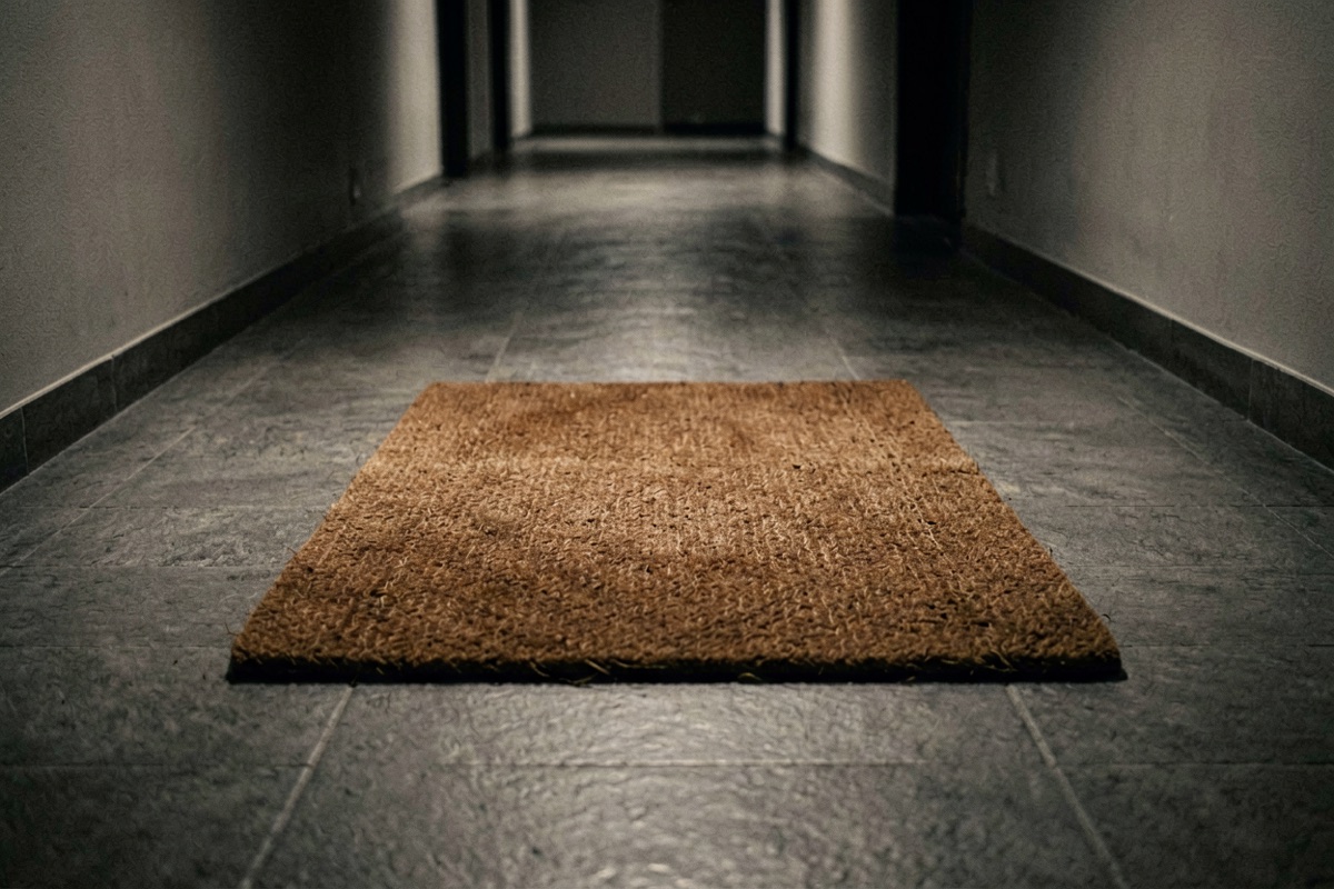 A worn brown doormat on tiled flooring outside a flat door (AI-generated illustration)