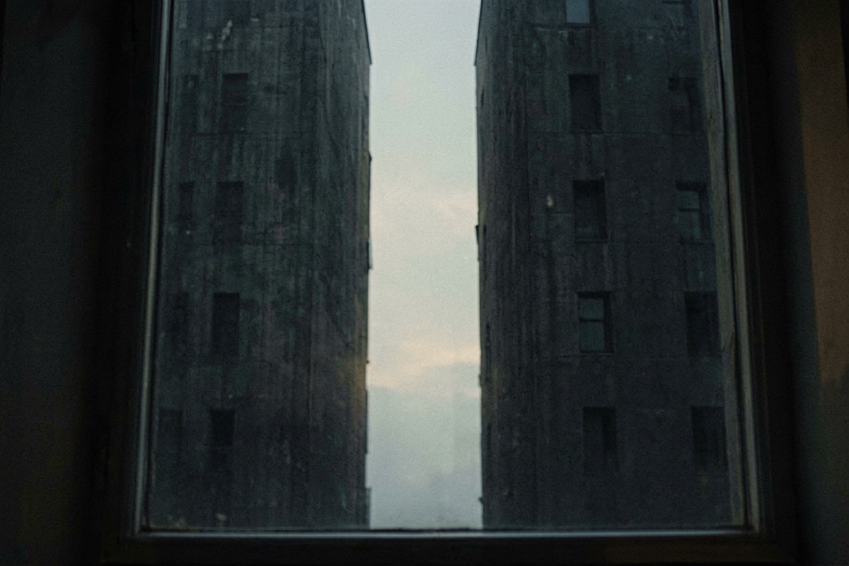 A narrow slot of pale sky between two dark tower blocks seen from a window (AI-generated illustration)